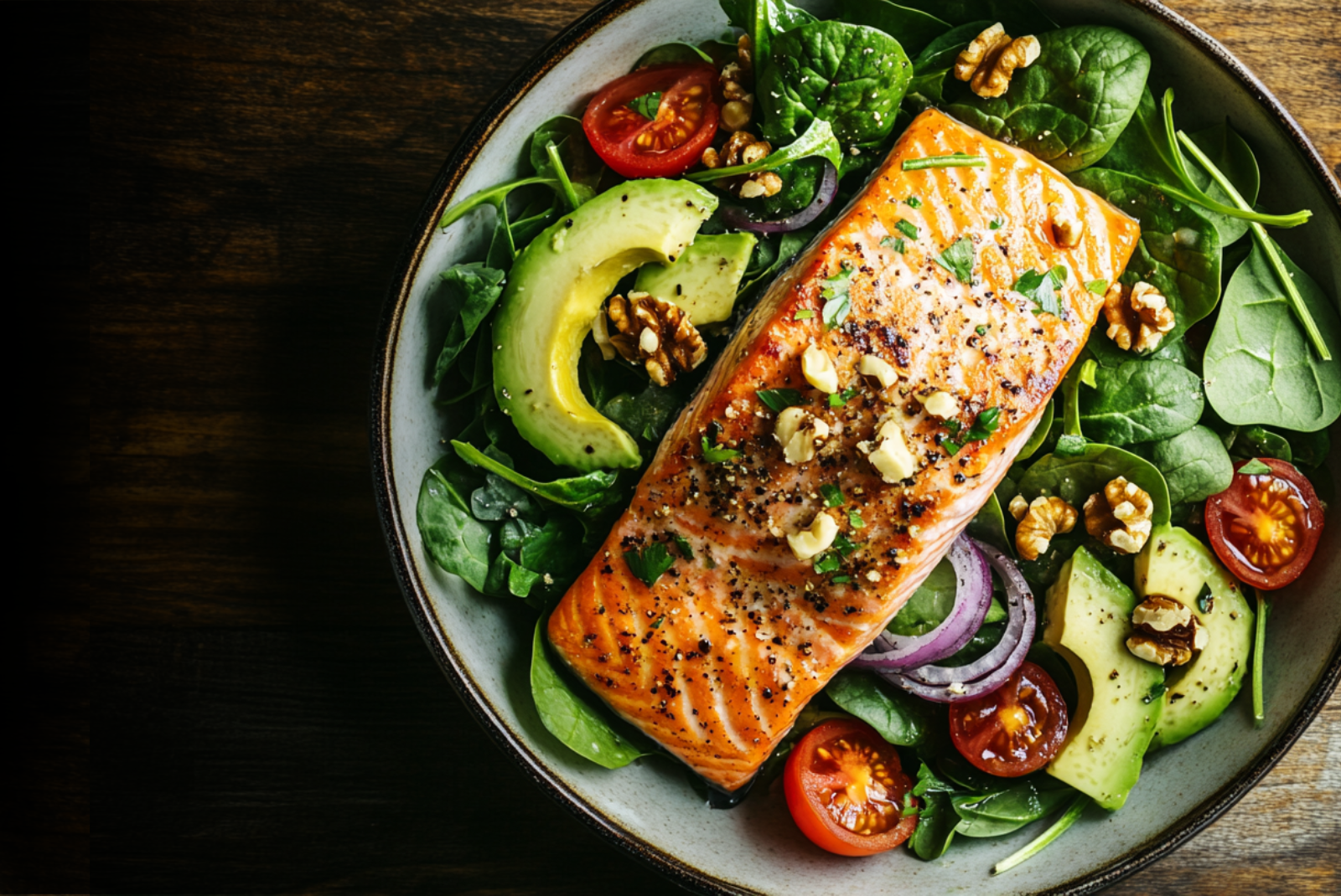 A fillet of salmon a bed of baby spinach with sliced cherry tomatoes, avocado, and red onions.